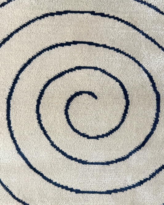 Detail of the Fitzroy rug, Edition 03: navy bamboo silk spiral, lustrous against the matte cream ground