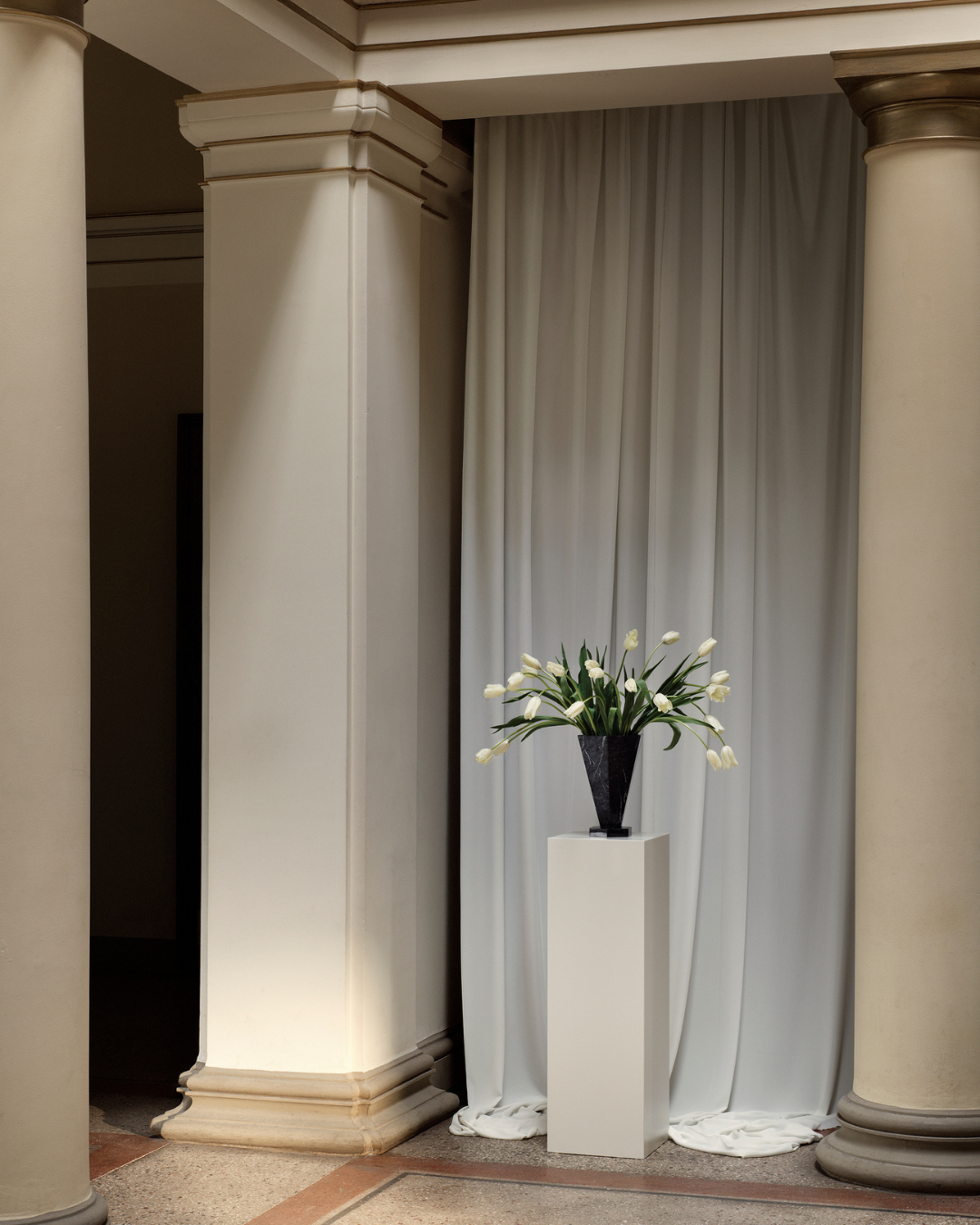 Black Marquina marble vase XL by Studio Vraco styled with white tulips on a plinth in a neoclassical interior