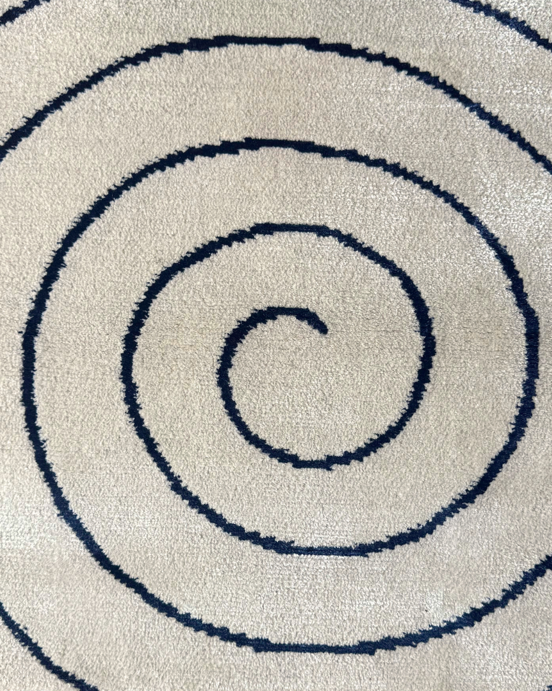 Detail of the Fitzroy rug, Edition 03: navy bamboo silk spiral, lustrous against the matte cream ground