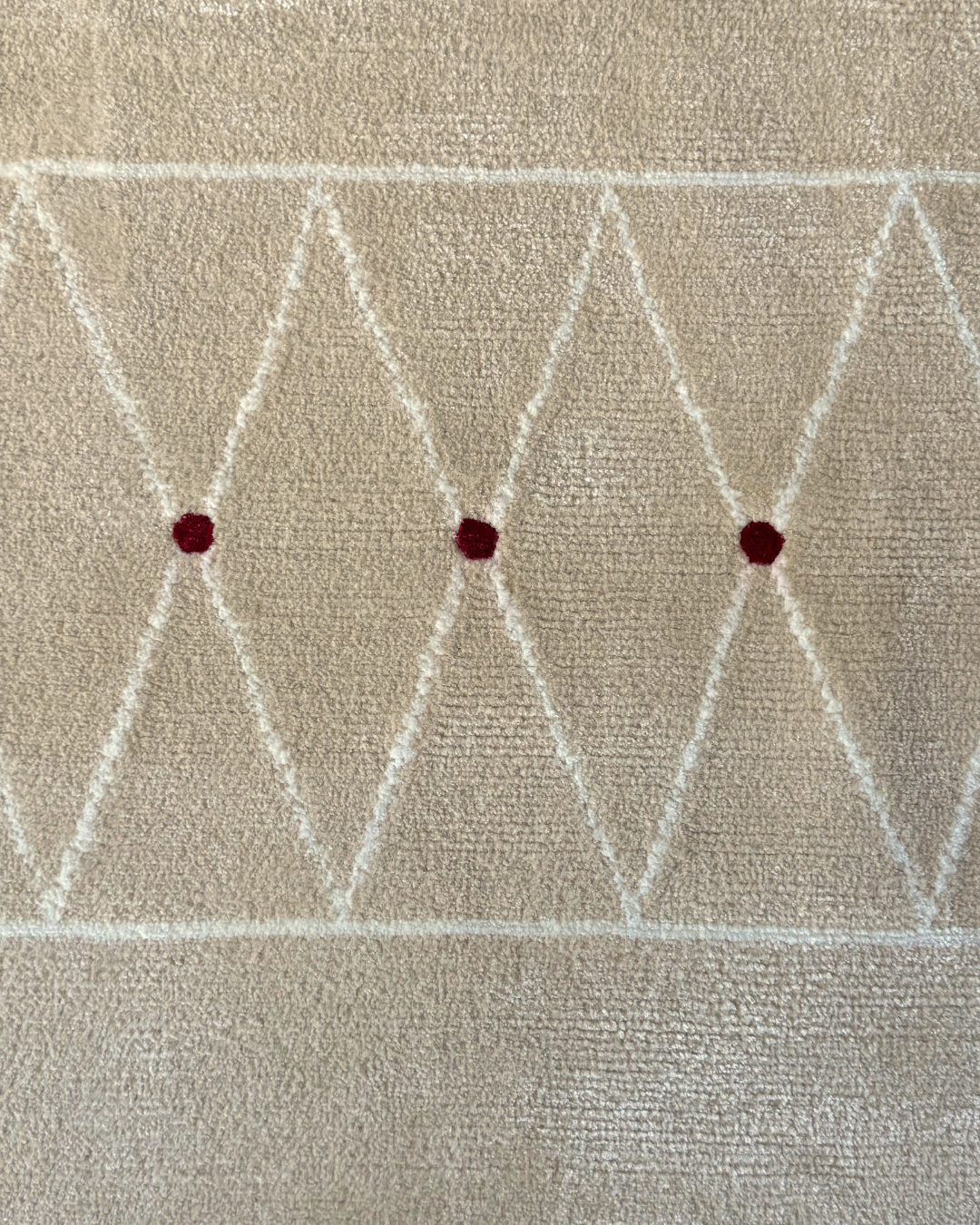 Detail of the Jacques rug, Edition 03: ivory treillage band with three deep crimson points on an oatmeal ground