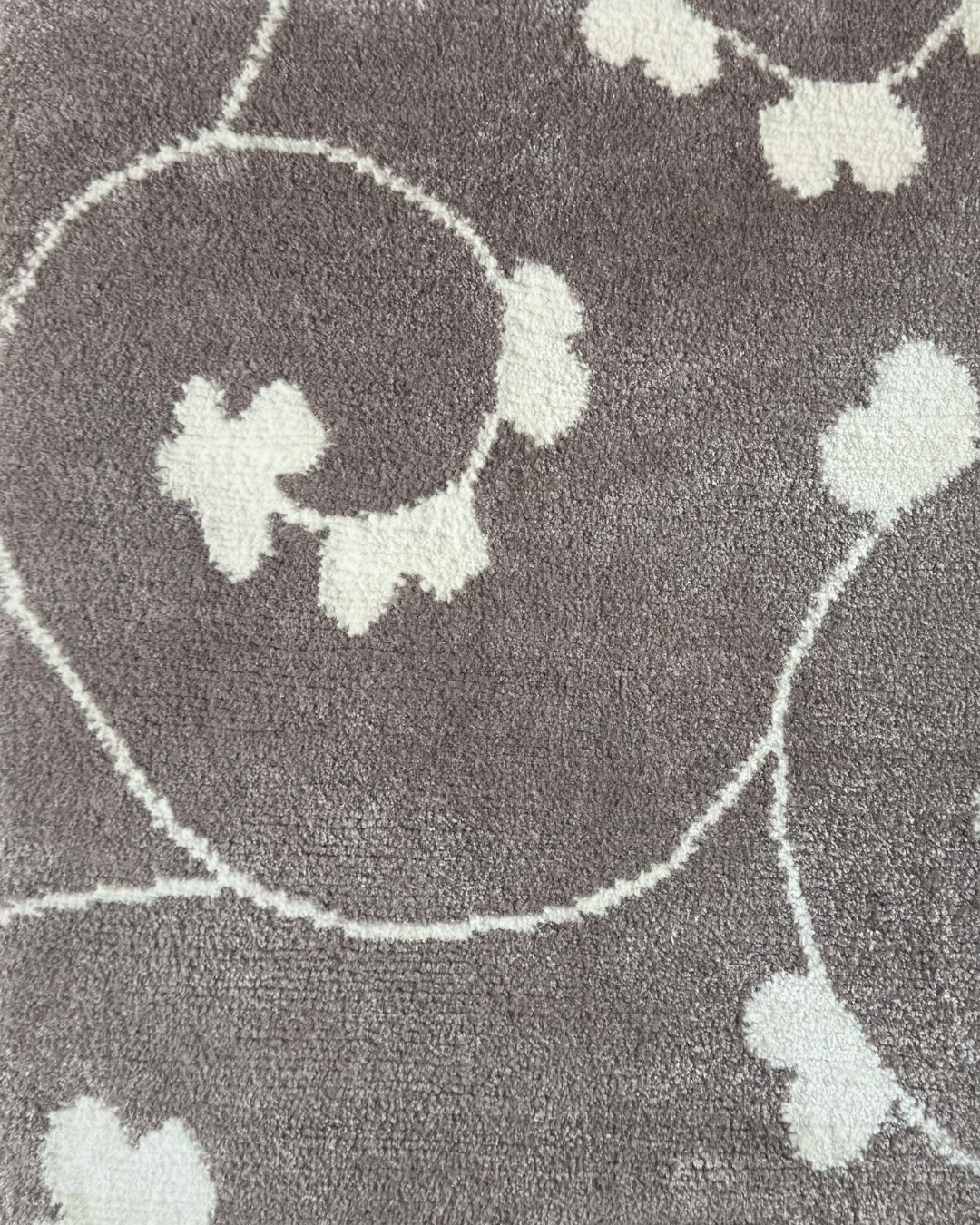 Detail of the Jardin rug, Edition 03: white trefoil blossom and vine hand-knotted on a warm grey ground