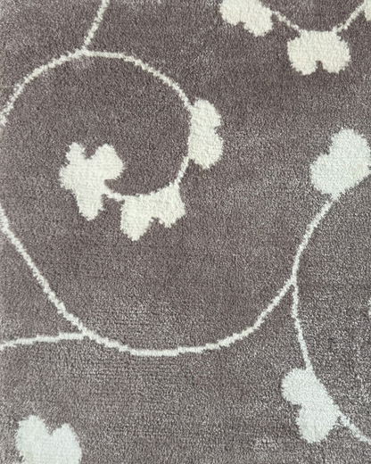 Detail of the Jardin rug, Edition 03: white trefoil blossom and vine hand-knotted on a warm grey ground